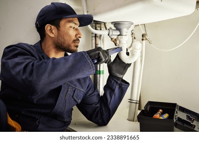 Plumbing, pipes and maintenance with man in kitchen for repair, industrial and inspection. Handyman, tools and safety with male plumber fixing sink for home improvement, drainage and water system