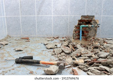 Plumbing problems. A wall of a bathroom is opened to find a leak from a pipe leaving rubble on the floor.