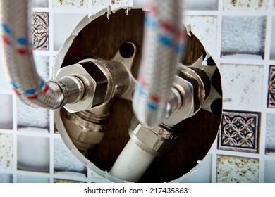 Plumbing system, connector of braided hose water pipe for supplying hot and cold water to home comes out of hole in wall of house in countryside.