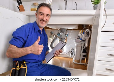 Plumbing technician checking water installation under the sink of a home kitchen with notepad and hand with ok gesture. Horizontal composition. - Powered by Shutterstock
