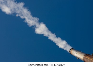 a plume of smoke or steam from an industrial smokestack on a clear blue sky.