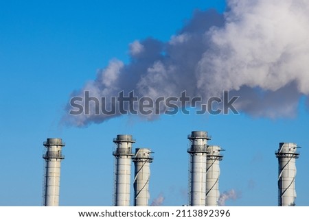 Plumes of smoke, gasses and steam billowing from a series of industrial smoke stacks against a blue sky