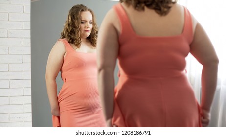 Plump female looking in mirror, upset about her belly, overweight insecurities
