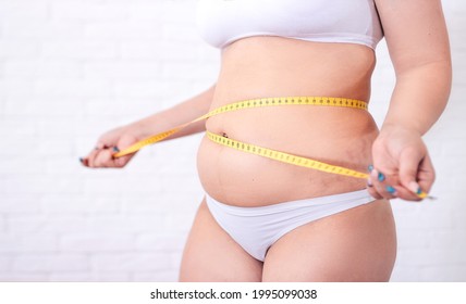 A Plump Woman With A Tape Measure Tape A Centimeter Around Her Waist. Woman Measures Her Waist Fat Tummy.