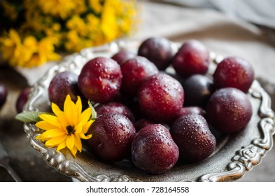 
Plums on a beautiful metal plate with a yellow flower.