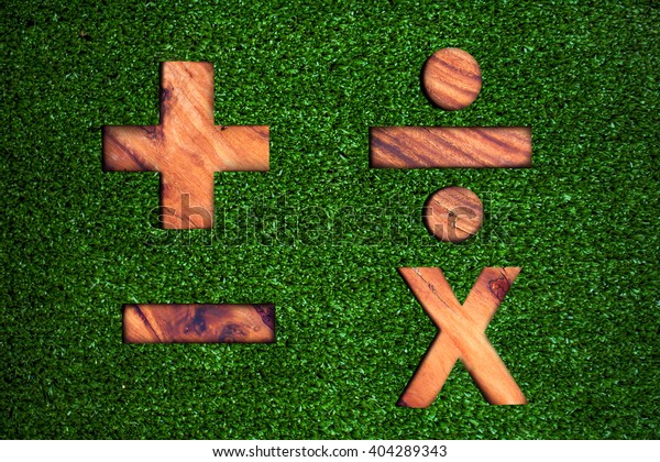 plus minus multiply divide\
text concept on wooden texture over artificial grass\
background.