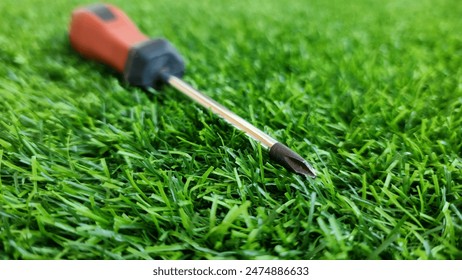 A plus screwdriver with a magnetic tip and a red rubber handle on a green grass background