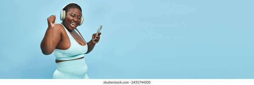 plus size african american woman listening music in headphones connected to smartphone, banner - Powered by Shutterstock