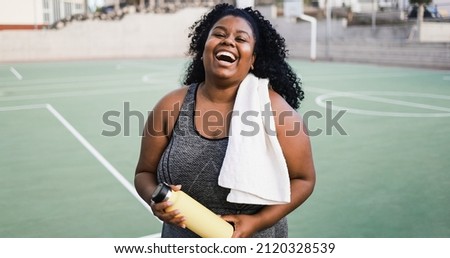 Plus size african woman smiling at camera while doing running routine outdoor - Soft focus on face