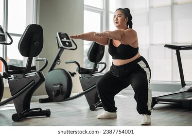 Plus size Asian woman exercises in gym. Beautiful overweight woman in sportswear doing squat exercise in fitness. concept of body positive, self-acceptance, weight loss. - Powered by Shutterstock