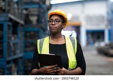 Plus Size Black Female Worker Wearing Safety Hard Hat Helmet Inspecting Old Car Parts Stock While Working In Automobile Large Warehouse