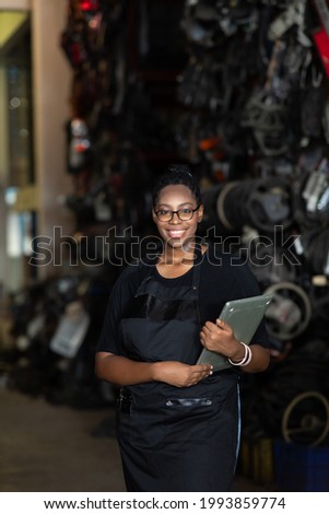 Plus size black female worker inspecting old car parts stock while working in automobile large warehouse