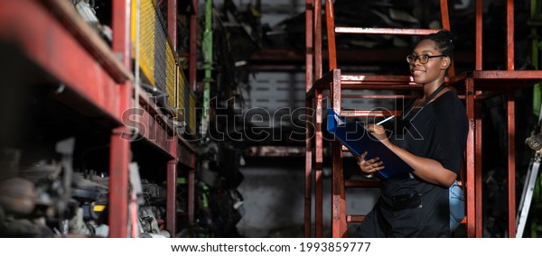 Plus size black\
female worker inspecting old car parts stock while working in\
automobile large warehouse