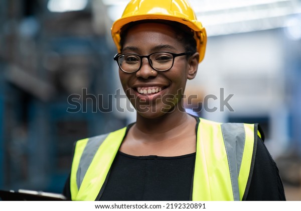 Plus size black female worker wearing safety
hard hat helmet inspecting old car parts stock while working in
automobile large warehouse
