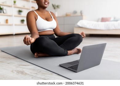 Plus Size Black Woman Having Online Meditation Or Yoga Class, Sitting In Lotus Pose Next To Laptop At Home, Cropped View. Unrecognizable Overweight Young Lady Doing Breathing Exercises Indoors