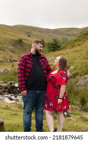 Plus Size Couple Outside On An Adventure Looking Into Each Other’s Eyes. Female Wearing A Red Dress.