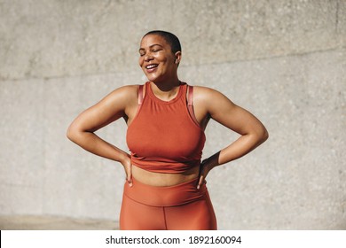Plus size female model in sportswear smiling with her hands on hips. Positive woman relaxing after workout outdoors.