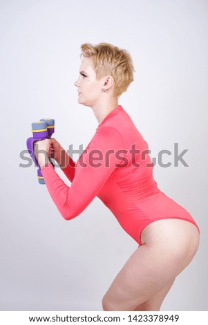 plus size girl with short hair and big breasts in red spandex sports bodysuit doing exercises with purple dumbbells on white background in Studio alone