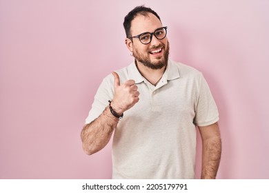 Plus size hispanic man with beard standing over pink background doing happy thumbs up gesture with hand. approving expression looking at the camera showing success. 