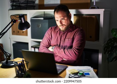 Plus size hispanic man with beard working at the office at night skeptic and nervous, disapproving expression on face with crossed arms. negative person. 