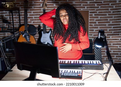 Plus Size Hispanic Woman Playing Piano At Music Studio Confuse And Wonder About Question. Uncertain With Doubt, Thinking With Hand On Head. Pensive Concept. 