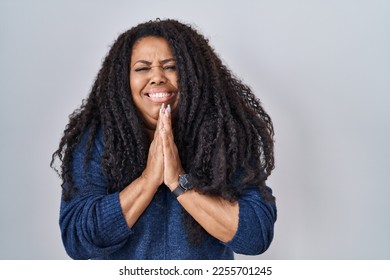 Plus size hispanic woman standing over white background praying with hands together asking for forgiveness smiling confident.  - Shutterstock ID 2255701245
