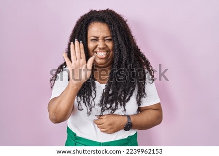 Plus size hispanic woman standing over pink background waiving saying hello happy and smiling, friendly welcome gesture 