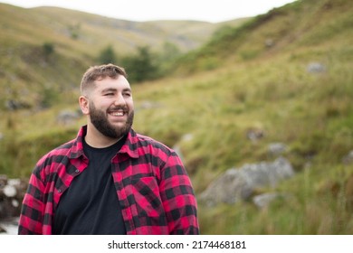 Plus size male wearing a red and black checker shirt staring off and smiling with a hilly green background - Shutterstock ID 2174468181
