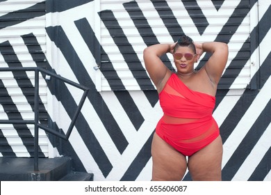 Plus size model in a red bikini against a black and white striped background