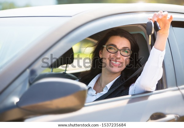 Plus size model\
sitting at the wheel of own car and shows the keys. Buying or\
renting a car in the\
showroom