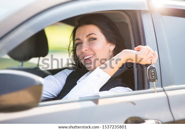 Plus size model\
sitting at the wheel of own car and shows the keys. Buying or\
renting a car in the\
showroom