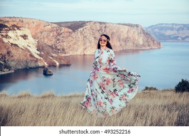 Plus Size Model Wearing Floral Maxi Dress Posing In Field. Young And Fashionable Overweight Woman Walking On The Shore.