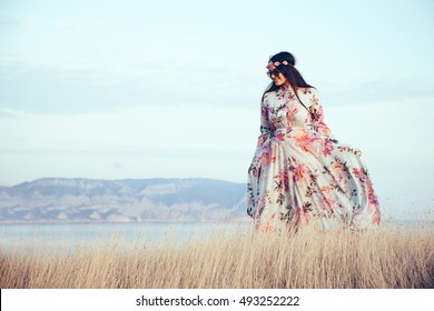 Plus size model wearing floral maxi dress posing in field. Young and fashionable overweight woman walking on the shore. - Shutterstock ID 493252222