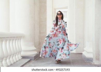 Plus size model wearing floral maxi dress posing on the city street. Young and fashionable overweight woman walking around town.