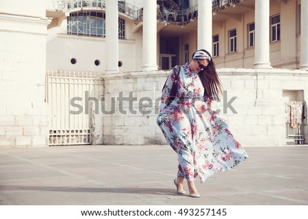 Plus size model wearing floral maxi dress posing on the city street. Young and fashionable overweight woman walking around town.