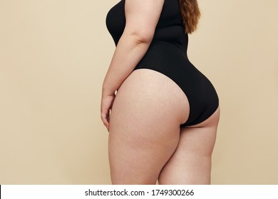Plus Size Model. Woman Hips Close Up. Big Torso In Black Bodysuit. Full-figured Female Posing On Beige Background. Body Positive Concept.