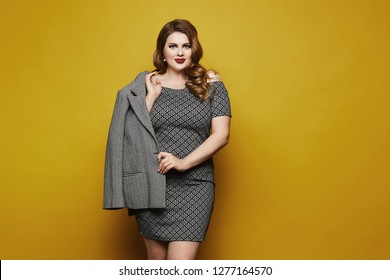 Plus size sexy model girl, fashionable blonde with bright makeup and with stylish hairstyle, in the dress with geometric patterns posing at the yellow background in a studio, isolated