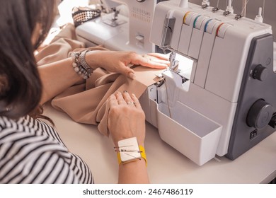 A plus size woman fashion designer uses an overlock sewing machine in her studio. A seamstress sews clothes in her sewing workshop.