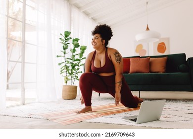 Plus size woman following workout video on laptop and doing home workout. Happy female in workout wear stretching at home. - Powered by Shutterstock
