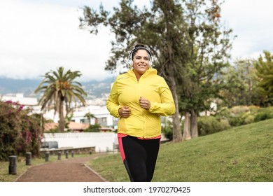 Plus size woman jogging outdoor at city park - Main focus on headphones - Powered by Shutterstock