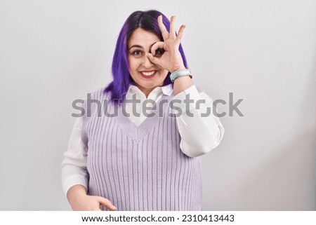 Plus size woman wit purple hair standing over white background doing ok gesture with hand smiling, eye looking through fingers with happy face. 