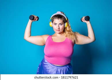 Plus Size Young Black Woman Weight Lifting On Blue Background Listening Music - Isolated Diverse Caucasian Female Workout With Weights Wearing Headphones - Body Positive, Training, Sport Concept