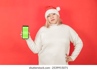 Plus size young woman portrait in santa hat holding green screen sumrtphone on red background. - Powered by Shutterstock