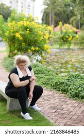 Plus Size Young Woman Resting On Bench After Morning Jog And Checking Heart Rate On Fitness Tracker