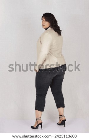 A plus sized beautiful female model posing in beige leather jacket in style with high heels and black jeans along orange bag 