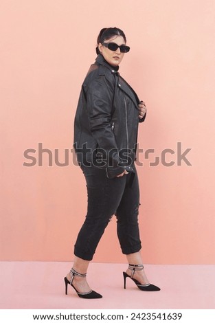 plus sized female model posing in black leather jacket and black jeans with glasses and high heels 