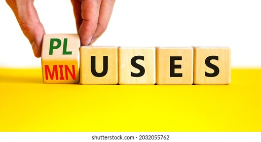 Pluses and minuses symbol. Businessman turns a wooden cube and changes the word 'minuses' to 'pluses'. Beautiful yellow table, white background. Business, pluses and minuses concept, copy space.