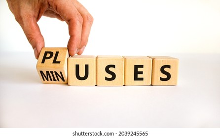 Pluses and minuses symbol. Businessman turns a wooden cube and changes the word 'minuses' to 'pluses'. Beautiful white table, white background. Business, pluses and minuses concept, copy space.