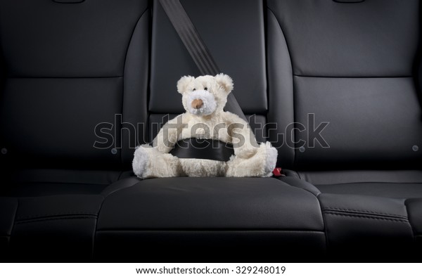 plush bear\
buckled  in the center of car back\
seat