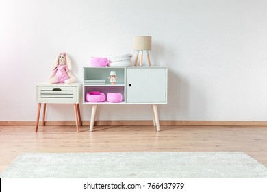 Plush Rabbit On White Bedside Cabinet Next To Cupboard With Lamp And Pink DIY Bags In Child's Room